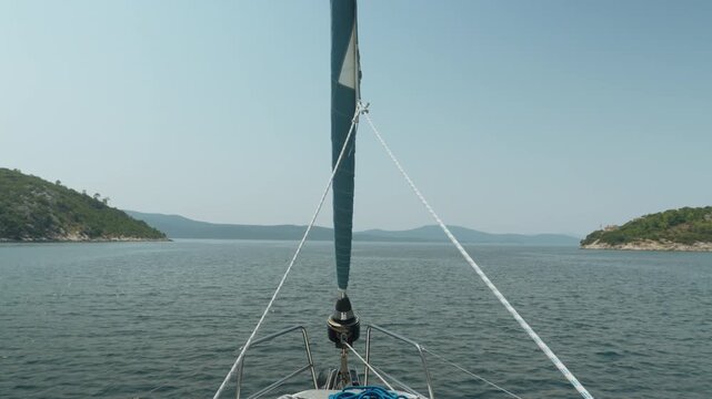 Sailboat Navigates Tranquil Bay With Distant Island In Sight. Gentle Sailing Adventure Across Calm Seas Towards Distant Island Horizon On Peaceful Summer Day