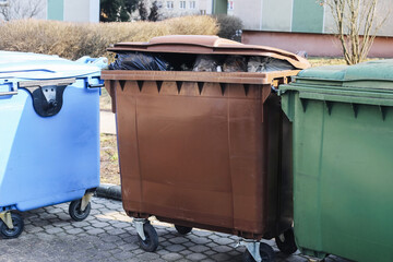 Large municipal garbage containers on wheels standing outdoors in residential area. Blue brown and green waste bins for household trash collection. Urban sanitation and recycling management concept.