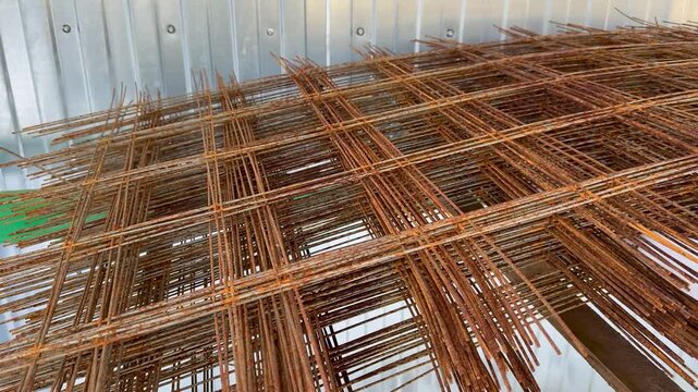 Stack rusty rebar rods closeup showing oxidized metal grid texture, outdoor storage lot with tied bundles and overlapping mesh.