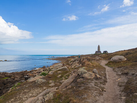 Camino de pista con rocas al lado del mar azul llegando al Phare du Cap L&eacute;vi en Carentan, viajando por la Normand&iacute;a Francesa en verano de 2022
