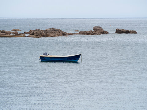 Vista mar&iacute;tima de una barca solitaria sobre el agua azul , al fondo rocas y el horizonte el el puerto de Barfleur, viajando por la Normand&iacute;a en Francia