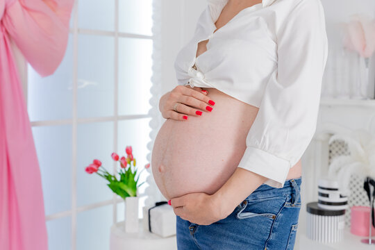 belly of caucasian pregnant woman in light room with flowers in the interior. Female gift, housewarming concept, health.Seventh month of pregnancy. parenthood and expectation concept.