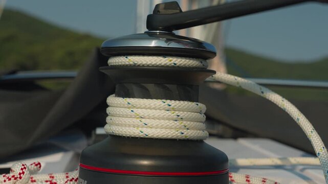 Focused Shot Of Nautical Winch Wrapped In Woven Rope On Boat. Close Detailed Image Capturing Sailboat Winch With Intertwined Braided Textured Rope Behind Island Hills