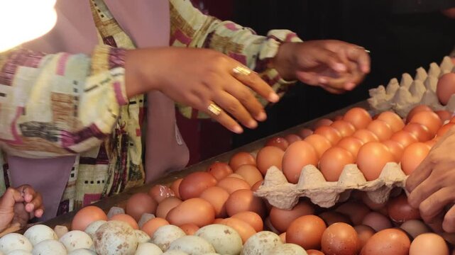 Close up of a woman choosing fresh brown chicken eggs from cardboard trays at a traditional market stall for daily grocery shopping.
