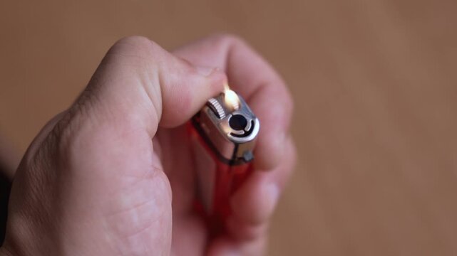 Close-up view of a hand repeatedly trying to light a red disposable lighter. The flint sparks multiple times, but the gas fails to ignite, representing a malfunctioning or empty object