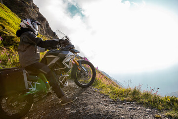 Motorcycle rider posing in Italian Alps during sunrise, dramatic sky. Travel and freedom, outdoor activities