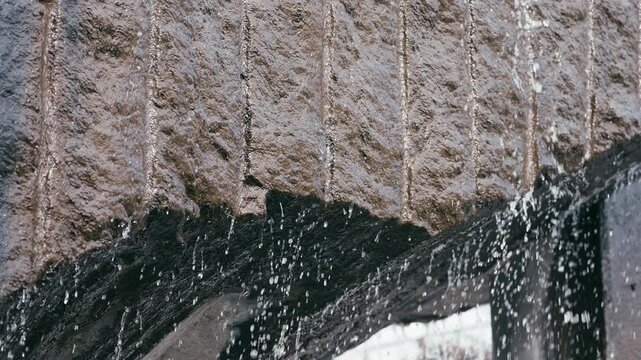 Straight lines of water flowing down a large slab of decorate rock.
