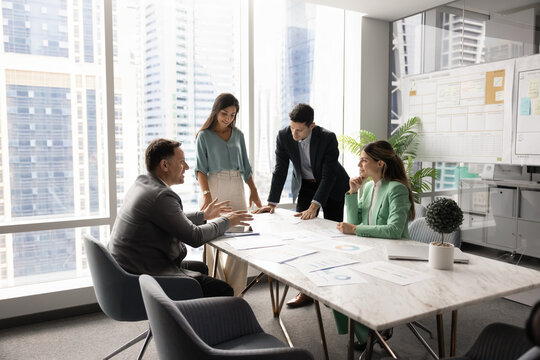 Multiethnic company managers startup developers team with middle aged leader boss gather around boardroom table brainstorming insights creating plans reviewing project materials in modern urban office