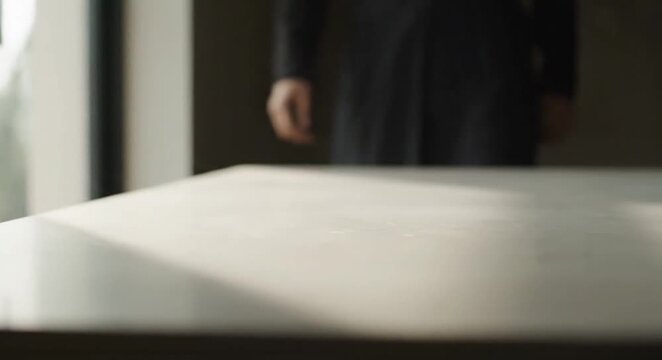 Sunlight and shadows cast diagonally across a clean, empty modern table surface in a minimalist interior setting, creating a tranquil backdrop.