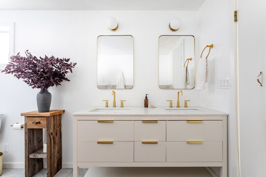 Modern bathroom interior with double vanity, brass fixtures and minimalist mirrors in bright contemporary residential home design