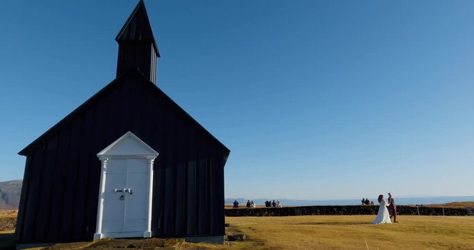 Just married young couple romantic bride and groom walk outside of the budakirkja black church in Iceland