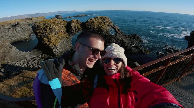 Happy smiling couple on honeymoon trip at Gatklettur - Arch Rock - cliff with natural arch near Arnarstapi, Snaefellsnes, West Iceland. Famous basalt Stone Arch.