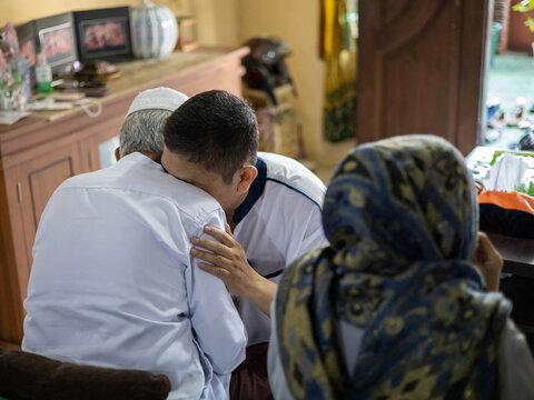 A touching moment of an Indonesian Muslim man traditionally asking for forgiveness (Sungkem) from his father during the Eid al-Fitr celebration.