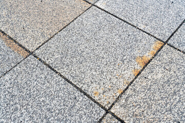 Close-up view of a textured gray stone pavement with visible dirt marks and light orange stains, showcasing urban infrastructure and surface wear, ideal for backgrounds in design.