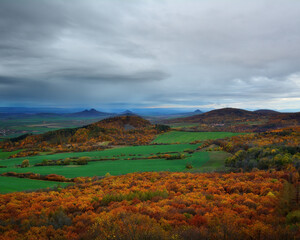 Colorful Autumn Forest and Green Fields under Stormy Sky