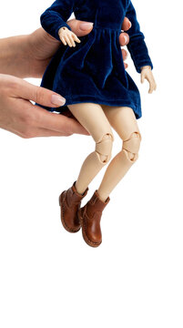 Human hands holding a ball-jointed doll wearing a blue velvet dress and brown boots isolated on a, transparent background