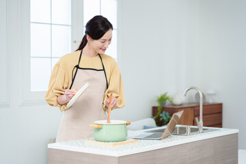 キッチンでパソコンを見ながら料理をする主婦