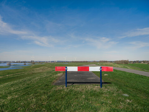 Red and white road barrier blocking dike road with flooded polder and wind turbines in background