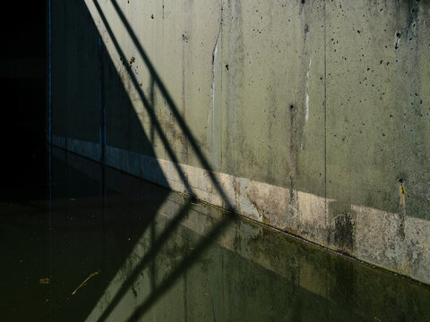 Abstract pattern of railing shadows on weathered concrete sluice wall with water and algae staining
