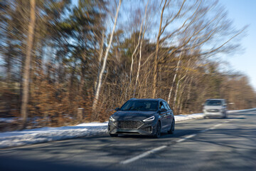 Fototapeta premium Modern wagon driving on snowy forest road with motion blur effect. Winter car on highway.