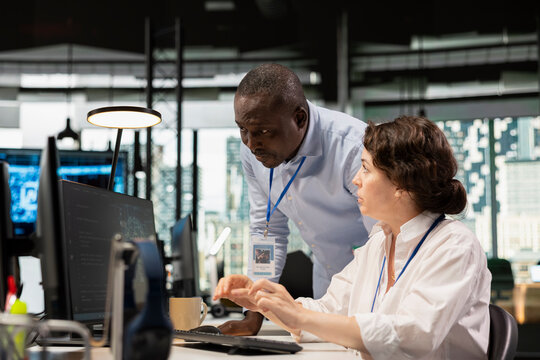 Manager supervising intern in office automating tasks using AI scripts on PC. Silicon Valley startup team leader overseeing employee using deep learning tech to speed up feature implementation