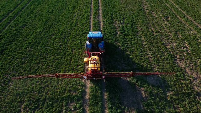 Aerial view of a blue tractor spraying a green field with a yellow sprayer.