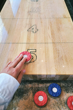 Player sliding shuffleboard disc toward scoring zone on wooden court