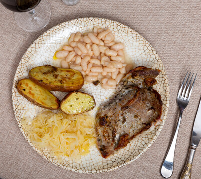 Hearty dish of roast pork served with fried potatoes, beans and sauerkraut