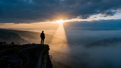 Obraz premium Lone figure on a cliff edge overlooking a misty landscape with dramatic sunbeams