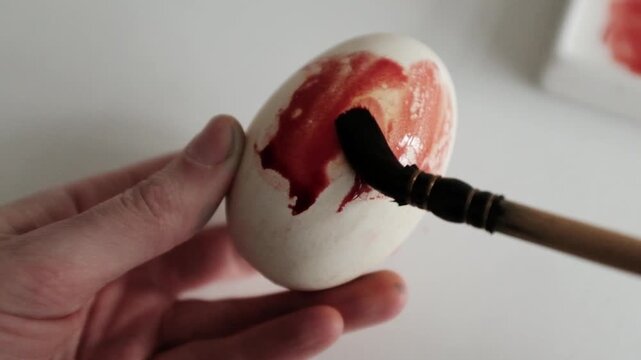 Close-up of the process of dyeing large goose eggs with red dye, showing hands coloring Easter eggs for spring holiday decorations and traditional DIY family crafts.
