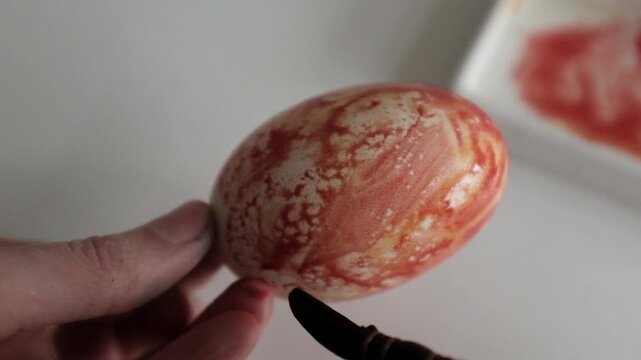 Close-up of the process of dyeing large goose eggs with red dye, showing hands coloring Easter eggs for spring holiday decorations and traditional DIY family crafts.