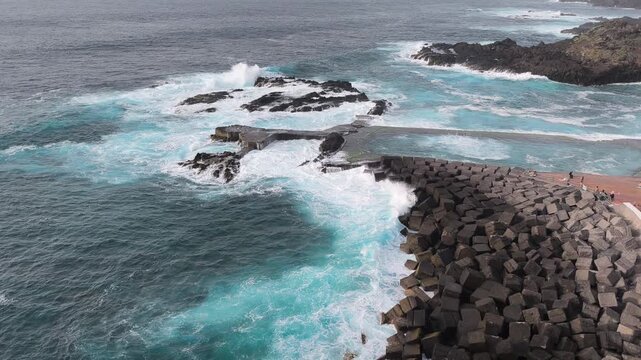 Aerial view of Atlantic waves hitting natural sea pool and coastal breakwater in Mesa del Mar, Tenerife, Spain. Dramatic ocean, volcanic coast and climate change concept