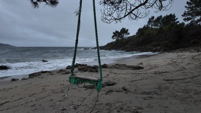 Empty handmade swing moving on a melancholy stormy beach