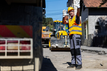 Construction worker giving directions on a busy street with machinery and equipment around in broad...