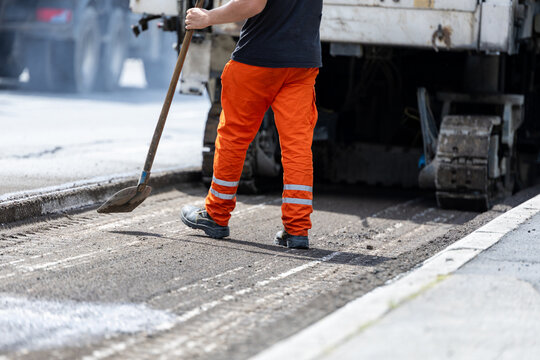Road worker operating asphalt milling machine removing old pavement from street