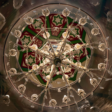Opulent crystal chandelier with intricate green Star of David motifs on red arabesque patterned ceiling, luxury Moroccan-Islamic interior design detail.