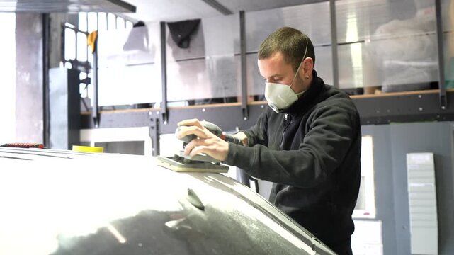 Body shop mechanic sanding a car roof with an electric tool
