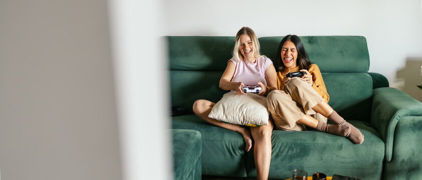 Women friends sharing a fun moment gaming at home, relaxing on a green sofa