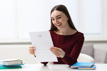 Obraz premium Smiling woman with acceptance letter from university at table indoors