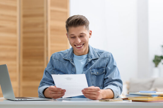 Happy man with acceptance letter from university at table indoors