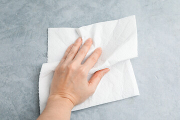 Woman wiping gray textured table with paper towel, top view