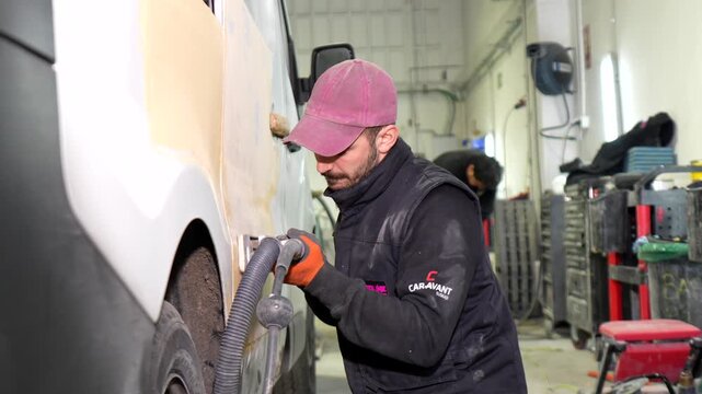 Auto body mechanic sanding car surface with orbital sander