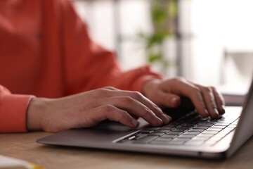 Woman working on laptop at wooden desk, closeup
