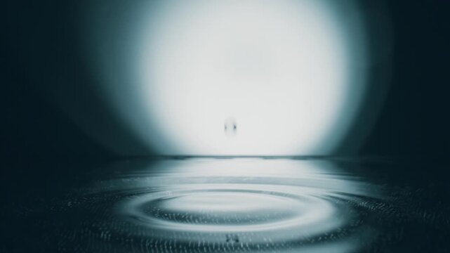 Macro shot of water drop falls down on grey transparent fluid surface creating water rings, slow motion