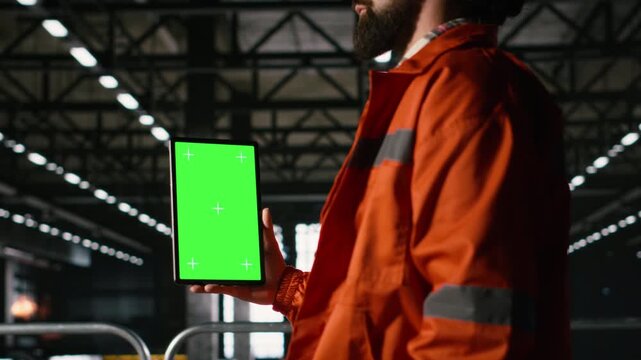 Tablet, vertical green screen, male engineer, heavy industry operations, machinery hall engineering focus on manufacturing process and production along large-scale industrial space.