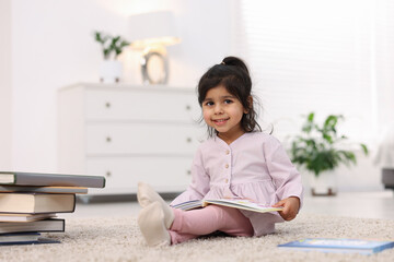 Fototapeta premium Cute little girl reading book on floor at home. Space for text