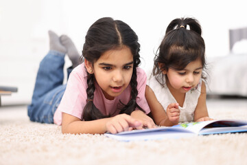 Fototapeta premium Cute little girls reading book together at home