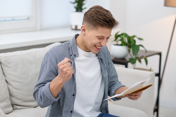 Smiling man with letter from university on sofa at home
