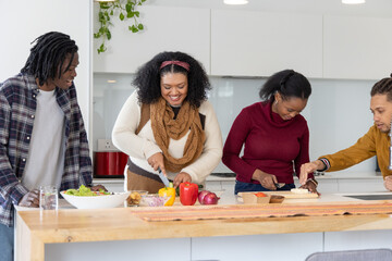 Diverse friends preparing meal, slicing yellow bell pepper with chef's knife on wooden island © wavebreak3
