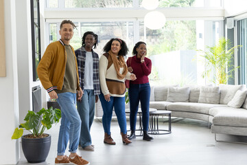 Obraz premium Diverse friends touring bright modern living room, pointing at sectional sofa and potted plants